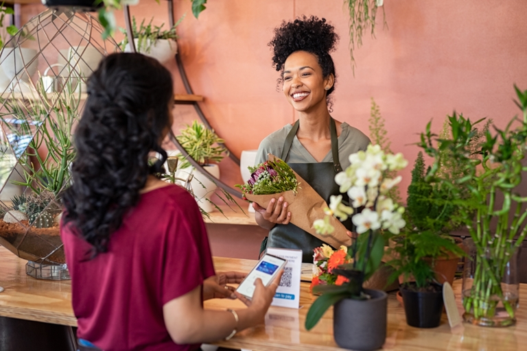 Friendly florist giving fresh bouquet to customer while they scan a QR code on there phone.