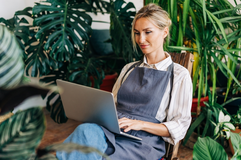 Saleswoman working on a laptop surrounded by plants.