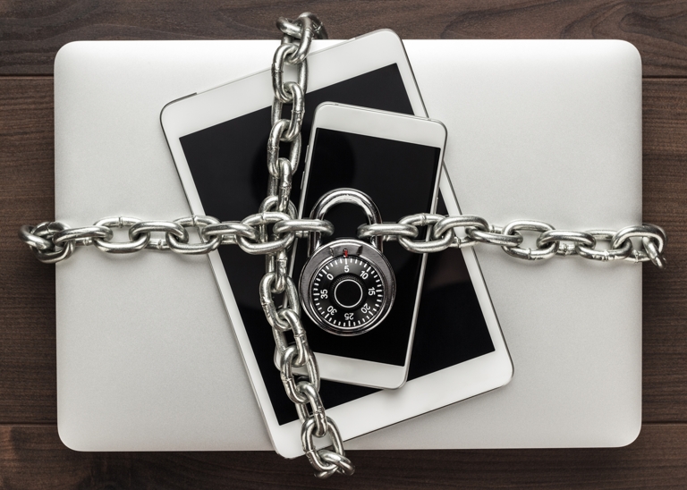 A laptop, tablet and phone wrapped in a chain with a lock on it.