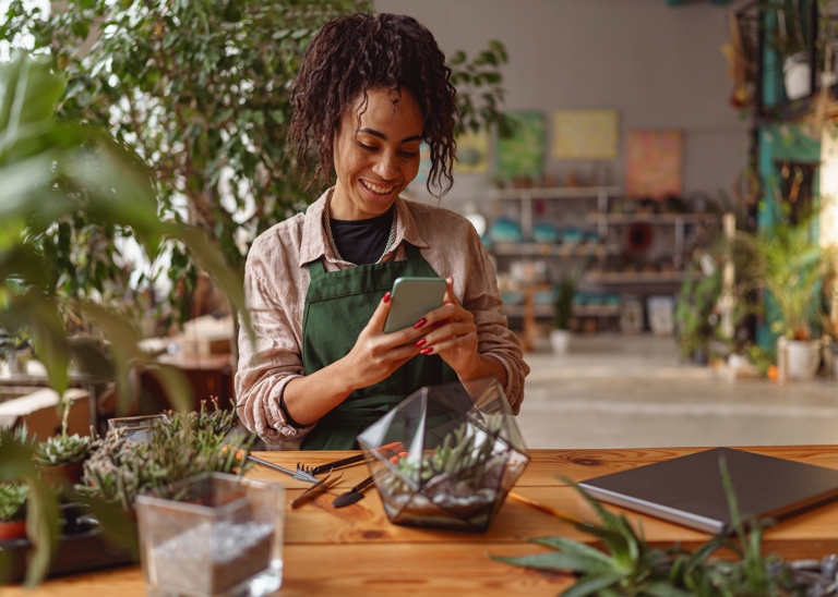 Smiling woman florist taking picture with her plants for publishing in social media.